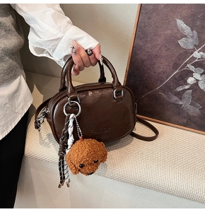 Detailed macro of dark brown leather cylinder bag with plush teddy bear charm and logo