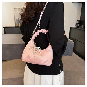Pink crescent shoulder bag featuring pleated handle and pearl bow charm detail