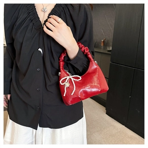 Detail of red ruched handle handbag with pearl bow charm and glossy leather texture