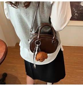 Detail of dark brown faux leather crossbody bag with teddy charm and silver zipper