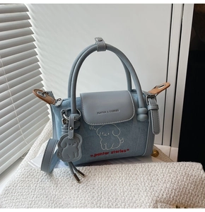 Close-up of denim blue dumpling bag with white dog embroidery and cute puppy charm