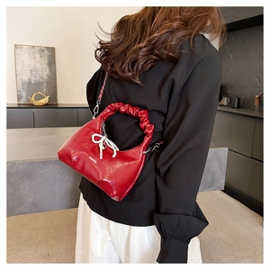 Detail of red patent leather dumpling bag with pleated handle and pearl bow charm
