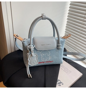 Detail of light blue denim handbag with cartoon dog embroidery and puppy charm