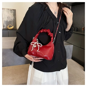 Close-up of red patent leather crescent bag with pearl bow charm and pleated handle