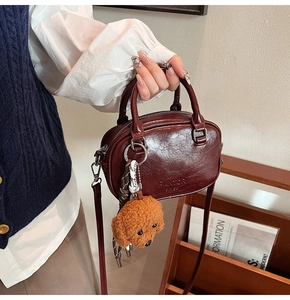 Detail of burgundy glossy handbag with FANTOR embossed logo and brown teddy bear charm