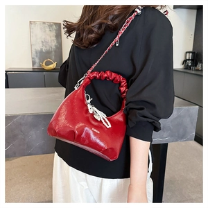 Detail of red glossy pleated handbag with pearl charm and metal chain strap