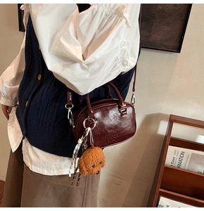 Detail of dark brown vintage leather handbag featuring a teddy bear charm and silk scarf