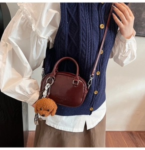 Detail of burgundy leather handbag with dog charm and embossed brand text on the front
