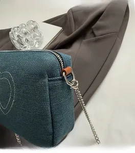 Close-up of blue washed denim heart embroidery bag with silver metal chain hook and zipper