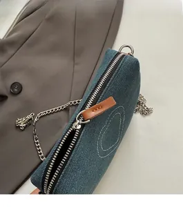 Detail of blue denim shoulder bag showing smooth silver zipper and leather puller