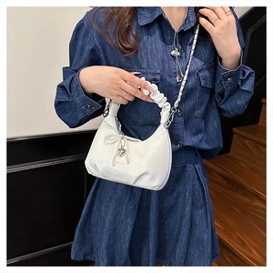 Detail of white glossy pleated bag featuring pearl bow, heart charm and silver chain