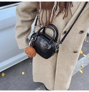 Detail of glossy black pleated crossbody bag with a brown plush puppy pendant charm