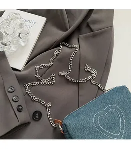 Detail of blue denim square bag with heart stitching and silver chain strap on grey blazer