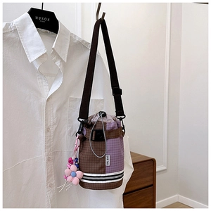 Detail of plaid bucket bag featuring drawstring closure and pink flower pendant accessory