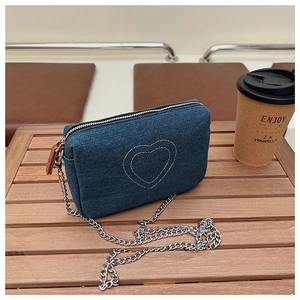 Close-up of heart embroidery on denim bag with chain strap on a wooden table