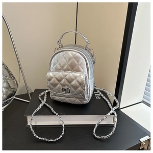Detail of silver quilted mini backpack with metal chain strap on minimalist background