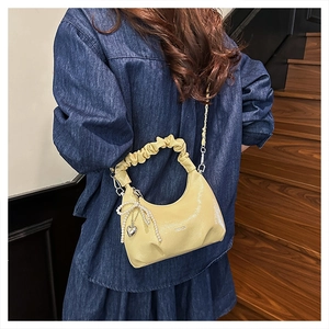 Detail of elegant cream yellow ruched dumpling bag with pearl bow and metal chain strap