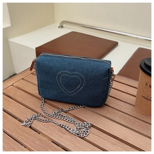 Close-up of vintage denim heart shoulder bag with silver chain strap on a wooden table
