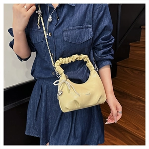 Detail showing creamy pleated handle and pearl bow charm on a fashion handbag