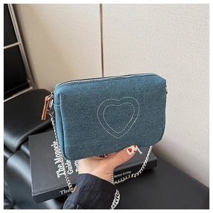 Detail of vintage washed denim crossbody bag featuring white heart embroidery and silver chain