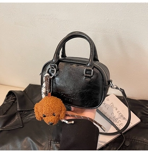 Detail of black vintage leather handbag with brown teddy charm and long strap