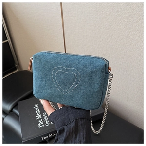 Detail of blue denim crossbody bag with white heart embroidery and metal chain strap