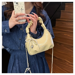 Detail of cream yellow crescent bag with pleated handle, pearl bow and chain strap