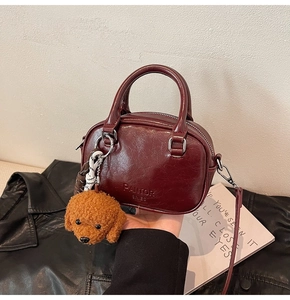 Detail of burgundy leather handbag with plush dog charm and embossed brand text