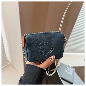 Detailed close-up of blue denim crossbody bag featuring white heart embroidery and silver chain