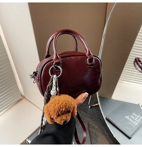 Detail of dark red faux leather mini handbag with teddy bear charm and woven strap accessory