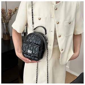 Detail of black quilted leather mini backpack with silver chain strap on beige outfit