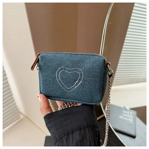 Detail of blue denim crossbody bag featuring white heart embroidery and metal chain