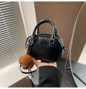 Close-up of black oil-wax texture Boston bag with brand lettering and teddy bear charm