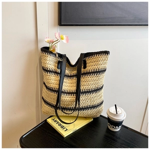 Détail d'un grand sac cabas en paille avec rayures noires et poignées en cuir sur table