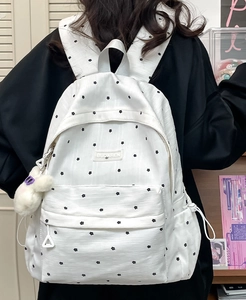 Detailed close-up of white polka dot backpack fabric with brand label and plush rabbit charm