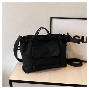 Détail d'un cabas en nylon noir montrant la poche à rabat avant et la large bandoulière