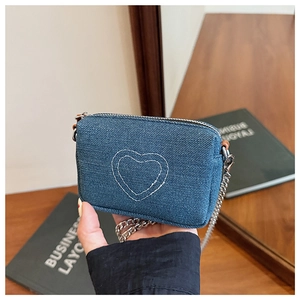 Macro shot of washed blue denim mini crossbody bag with white heart embroidery details