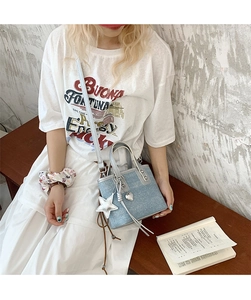 Blue denim bucket bag with star and heart charms shown in a lifestyle street setting