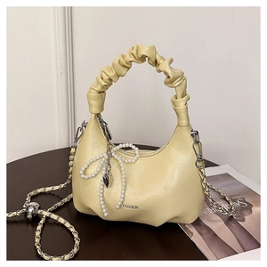 Detail of beige pleated handbag with pearl bow charm and elegant metal chain strap