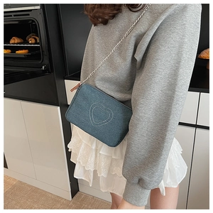 Detail of blue washed denim crossbody bag with white heart embroidery and silver chain strap