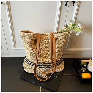 Détail d'un grand sac cabas en paille tissée avec rayures noires et anses en cuir marron