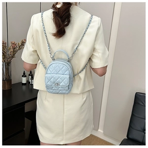 Rear view of a light blue quilted mini backpack with metal chain straps on a model