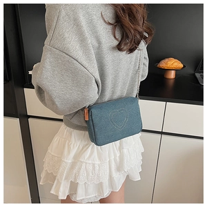 Detail of vintage blue denim crossbody bag featuring white heart embroidery and silver chain