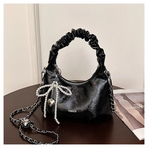 Detail of black glossy patent leather bag with large pearl bow and silver heart pendant