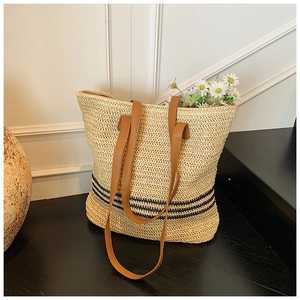 Détail du sac cabas en paille tressée avec anses en cuir et rayures noires décoratives