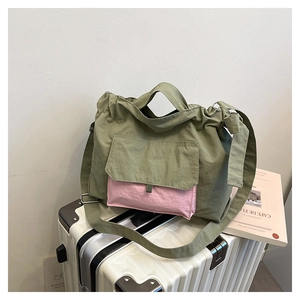 Détail du sac fourre-tout en nylon vert avec poche rose posé sur une valise blanche