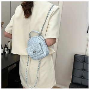 Back view of model wearing a light blue quilted mini backpack with leather chain strap