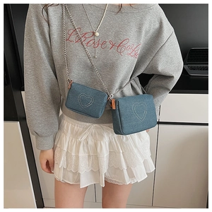 Detail of denim crossbody bag with heart embroidery and silver chain straps on model