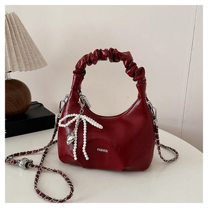 Detail of burgundy ruched dumpling bag featuring silver chain and pearl bow charm
