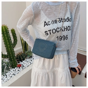 Detail of blue denim crossbody bag featuring heart embroidery and silver metal chain strap